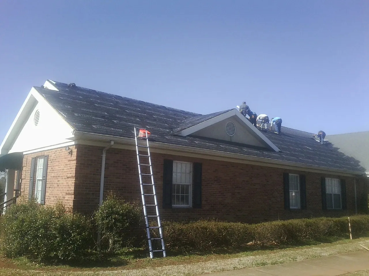 Crew tearing shingles off a brick ranch roof with a ladder set — Metal Roof Repair work by our crew in Parker