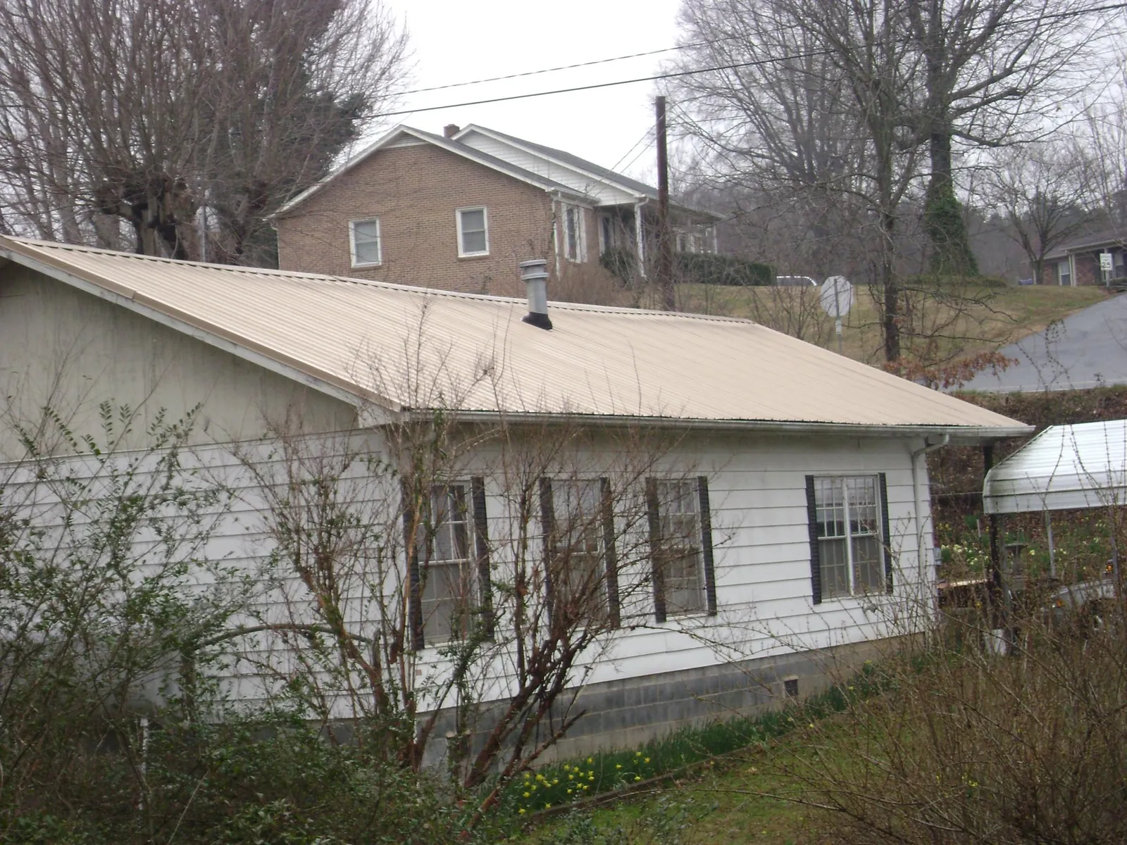 Tan metal roof on a white sided house set into a hillside — Commercial Roofing by Roofing Brothers in Parker